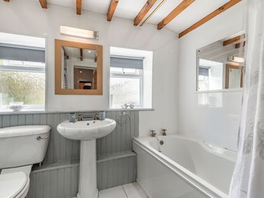 A bathroom with a toilet sink bathtub mirror and exposed wooden ceiling beams at Henrhiw Bach in Penmachno