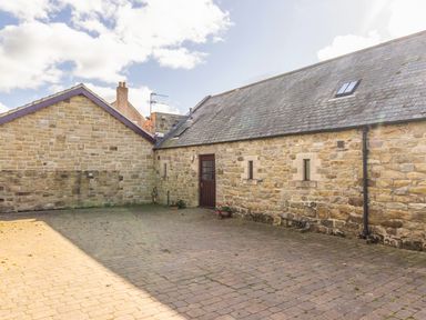 A paved courtyard surrounded by stone buildings with a wooden door and small windows at Ridge Cottage in Whitridge