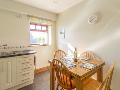A kitchen dining area with a wooden table set for four and a window with a vase on the sill at Ridge Cottage in Whitridge