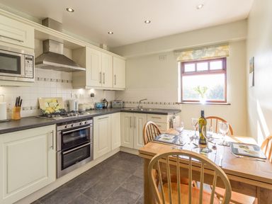 A kitchen with white cabinets a stove and oven a dining table set for four with wine glasses at Ridge Cottage in Whitridge