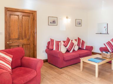 A sitting room with red sofas and striped cushions wooden door and a wooden coffee table at Ridge Cottage in Whitridge