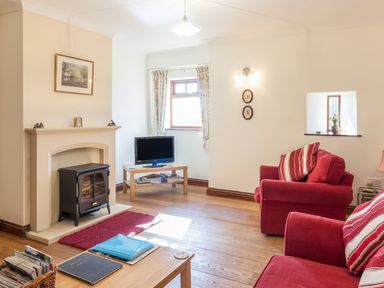A living room with a fireplace TV wooden furniture and red armchairs at Ridge Cottage in Whitridge