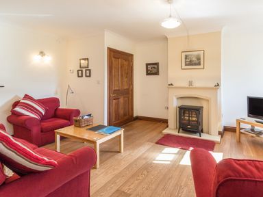 A living room with red sofas a wooden coffee table a fireplace and a television at Ridge Cottage in Whitridge