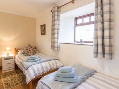 A bedroom with two single beds each with folded towels a bedside table with a lamp and a window with curtains at Ridge Cottage in Whitridge