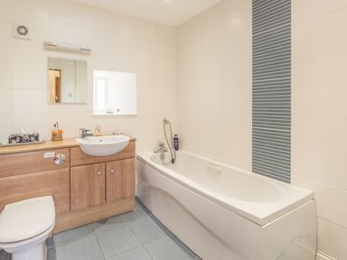A bathroom with a bathtub a sink a toilet and wooden cabinets at Ridge Cottage in Whitridge