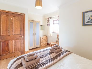 A bedroom with a wooden door a wardrobe a chest of drawers and a chair with towels on the bed at Ridge Cottage in Whitridge