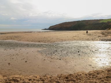 A sandy beach with a small stream flowing towards the sea and a hill in the background at Timbertwig Lodge in Lamphey near Pembroke