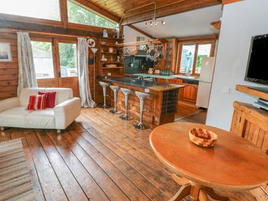 A living area with wooden floors a white couch with cushions a round wooden table and a kitchen with a breakfast bar and stools at Timbertwig Lodge in Lamphey near Pembroke