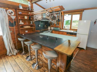 A kitchen with a countertop bar with stools hanging pots and pans stove and refrigerator at Timbertwig Lodge in Lamphey near Pembroke