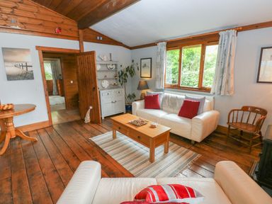 A living room with white sofas red cushions wooden coffee table and wooden flooring at Timbertwig Lodge Lamphey near Pembroke