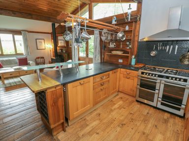 A kitchen with wooden cabinets hanging utensils and a stove next to a living room with sofas at Timbertwig Lodge in Lamphey near Pembroke