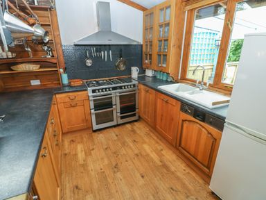 A kitchen with wooden cabinets a gas stove a double oven a sink under a window and a refrigerator at Timbertwig Lodge Lamphey near Pembroke