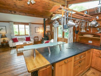 A kitchen with wooden cabinets and counter overlooking a living room with white sofas and red cushions at Timbertwig Lodge in Lamphey near Pembroke
