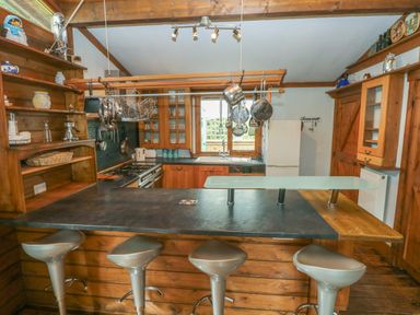 A kitchen with wooden cabinets a black countertop a window above the sink and four stools at the counter at Timbertwig Lodge Lamphey near Pembroke