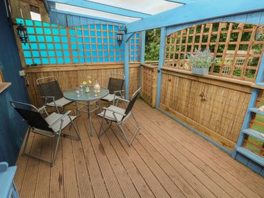A covered wooden deck with four chairs and a round glass table with flowers at Timbertwig Lodge in Lamphey near Pembroke