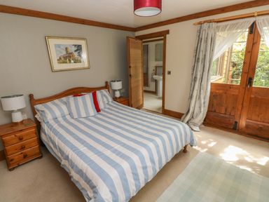 A bedroom with a double bed striped bedding wooden bedside tables and a door leading to a bathroom at Timbertwig Lodge Lamphey near Pembroke