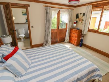A bedroom with a bed striped bedding a wooden dresser and an ensuite bathroom at Timbertwig Lodge Lamphey near Pembroke