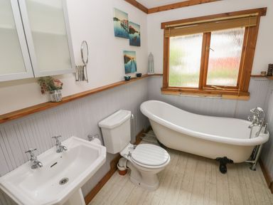 A bathroom with a clawfoot bathtub toilet sink and wooden framed window at Timbertwig Lodge Lamphey near Pembroke