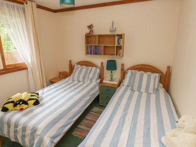 A bedroom with two single beds each with striped bedding a bedside table with a lamp and small shelf with books and toys at Timbertwig Lodge in Lamphey near Pembroke