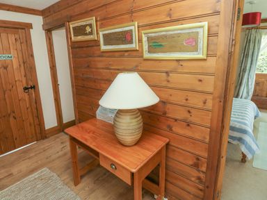 A wooden hallway with a table and lamp beside a door and a bedroom visible at Timbertwig Lodge in Lamphey near Pembroke