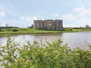 A stone castle ruin on grassy land beside a river with bushes in the foreground at Timbertwig Lodge in Lamphey near Pembroke