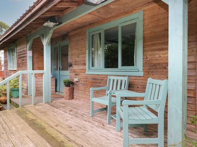 A wooden porch with two mint green chairs and a small table at Timbertwig Lodge in Lamphey near Pembroke