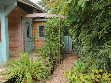 A wooden house with green doors and windows surrounded by plants and a gravel pathway at Timbertwig Lodge in Lamphey near Pembroke