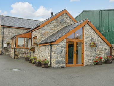 Stone building with wooden framed windows and doors surrounded by flower pots at Pendre Uchaf in Melin-y-Wig near Ruthin