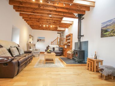 A living room with leather sofas a wood stove and wooden ceiling beams at Pendre Uchaf in Melin-y-Wig near Ruthin