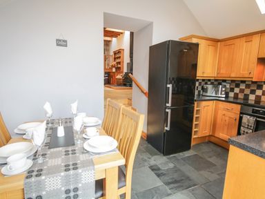 A kitchen with wooden cabinets black refrigerator and a dining table set with plates and glasses at Pendre Uchaf in Melin-y-Wig near Ruthin