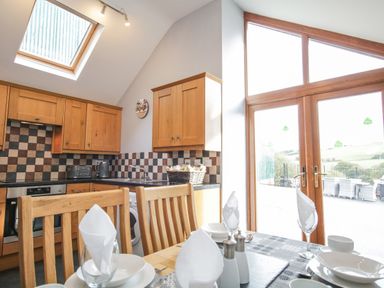 A kitchen with wooden cabinets and a dining table set near glass doors at Pendre Uchaf in Melin-y-Wig near Ruthin
