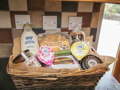 A basket with milk honey yogurt waffles butter and cheese on a kitchen counter at Pendre Uchaf in Melin-y-Wig near Ruthin