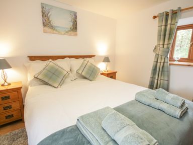 A bedroom with a made bed two bedside tables with lamps and a window with curtains at Pendre Uchaf in Melin-y-Wig near Ruthin
