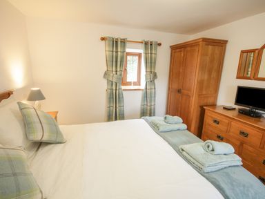 A bedroom with a bed with folded towels a wooden wardrobe and dresser with a TV at Pendre Uchaf in Melin-y-Wig near Ruthin