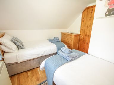 A bedroom with two single beds with blue throws and towels a wooden chest of drawers and a wooden door at Pendre Uchaf in Melin-y-Wig near Ruthin