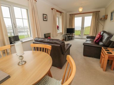 A living room with wooden dining table and chairs leather sofas and a television at White Rock Cottage in Beadnell