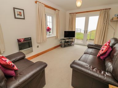 A living room with two leather sofas facing a television and glass doors at White Rock Cottage in Beadnell