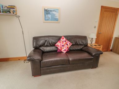 A leather sofa with two cushions in a living room with a wooden door and lamp at White Rock Cottage in Beadnell
