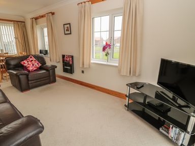 A living room with leather armchairs a TV on a stand and a window with curtains at White Rock Cottage in Beadnell