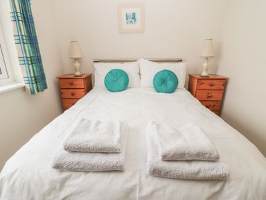 A bedroom with a bed with white sheets and two turquoise pillows two wooden bedside tables with lamps and towels on the bed at White Rock Cottage in Beadnell