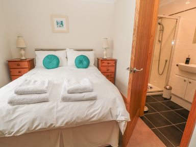 A bedroom with a double bed two bedside tables with lamps and an open door leading to a bathroom at White Rock Cottage in Beadnell