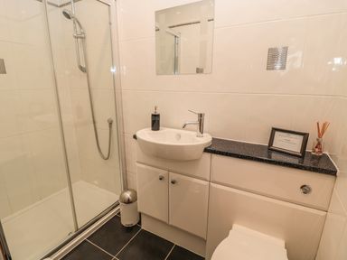 A bathroom with a shower enclosure sink with black countertop and cabinets at White Rock Cottage in Beadnell