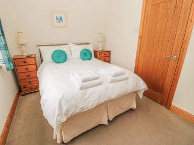 A bedroom with a double bed with white bedding and teal pillows two wooden nightstands with lamps and a wooden door at White Rock Cottage in Beadnell