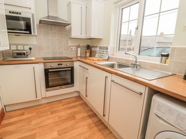 A kitchen with white cabinets wooden countertops an oven microwave toaster sink and washing machine at White Rock Cottage in Beadnell