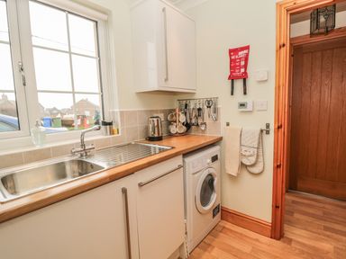A kitchen with a sink washing machine utensils and a wooden door at White Rock Cottage in Beadnell