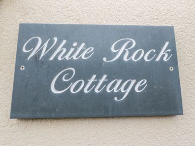 A stone plaque with White Rock Cottage written on it attached to a textured wall at White Rock Cottage in Beadnell