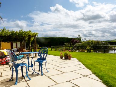 A patio with blue metal table and chairs next to a garden with plants and a pond at The Shippon Near Launceston