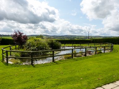 A garden with a fenced pond and plants with hills in the background at The Shippon Near Launceston