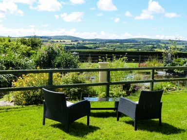 Two black chairs with a glass table on grass overlooking a fenced garden and countryside at The Shippon Near Launceston