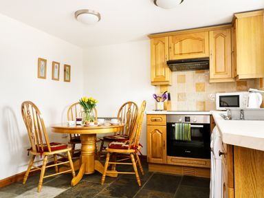 A kitchen with wooden dining table and chairs with tulips on the table and wooden cabinets at The Shippon Near Launceston